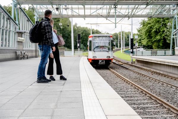 Foto: Zwei Personen warten auf dem Bahnsteig der Haltestelle Ruhr-Universität auf die gerade einfahrende U35 Bahn