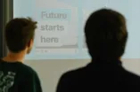 Foto: Zwei Personen schauen auf eine Leinwand, auf der steht "Future starts here".