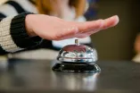 Klingel auf Platte, im Hintergrund eine Person, die auf die Klingel drückt.