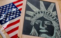 Auf einem Tisch liegen eine Amerika-Flagge und eine Schiefertafel, auf der der Kopf der Freiheitsstatue mit Kreide gezeichnet ist.