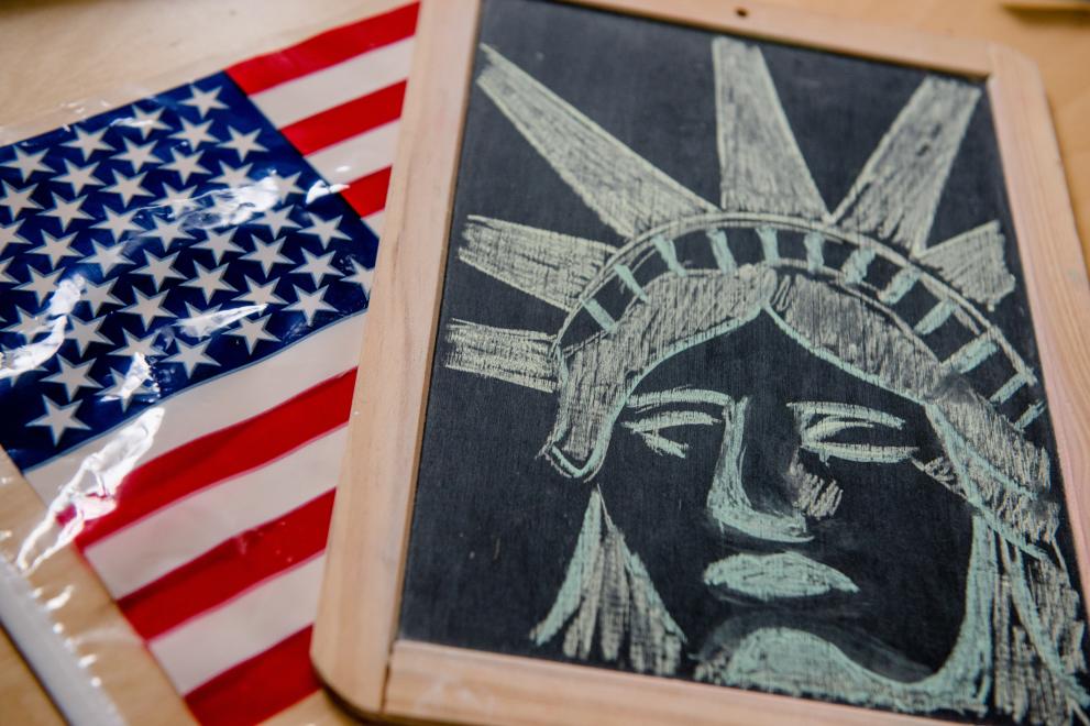 Auf einem Tisch liegen eine Amerika-Flagge und eine Schiefertafel, auf der der Kopf der Freiheitsstatue mit Kreide gezeichnet ist.