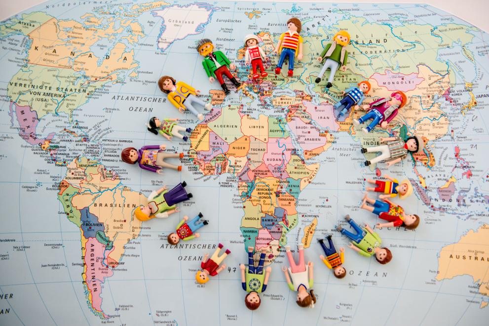 Weltkarte, auf der Playmobil-Figuren im Kreis nebeneinander liegen.