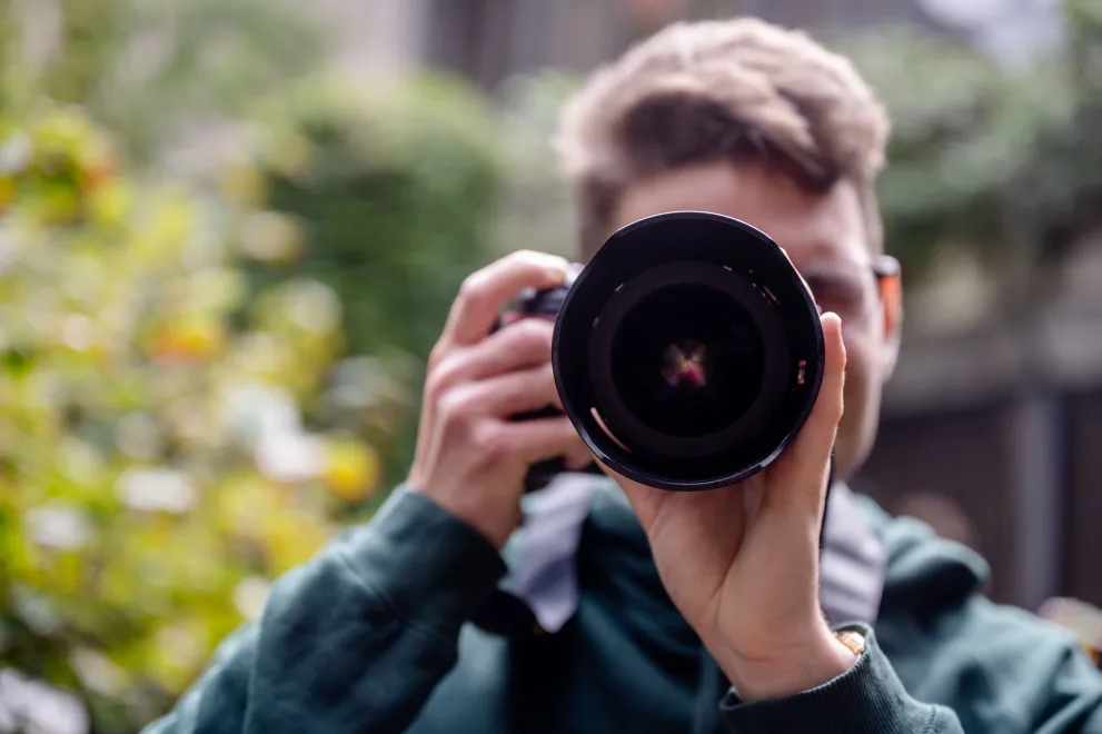 Eine Person hält die Kamera vors Gesicht und fotografiert in Richtung des Betrachters.