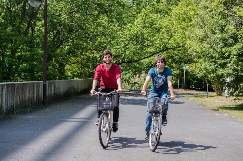 Zwei Studierende fahren Fahrrad auf dem Campus.