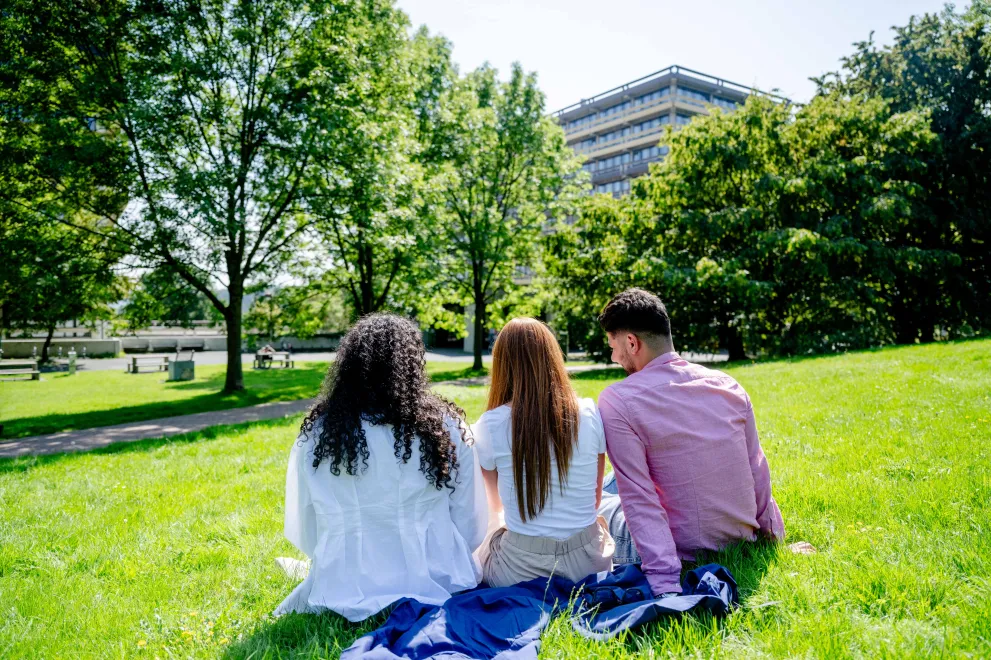 Drei Personen sitzen auf der Wiese vor der G-Reihe