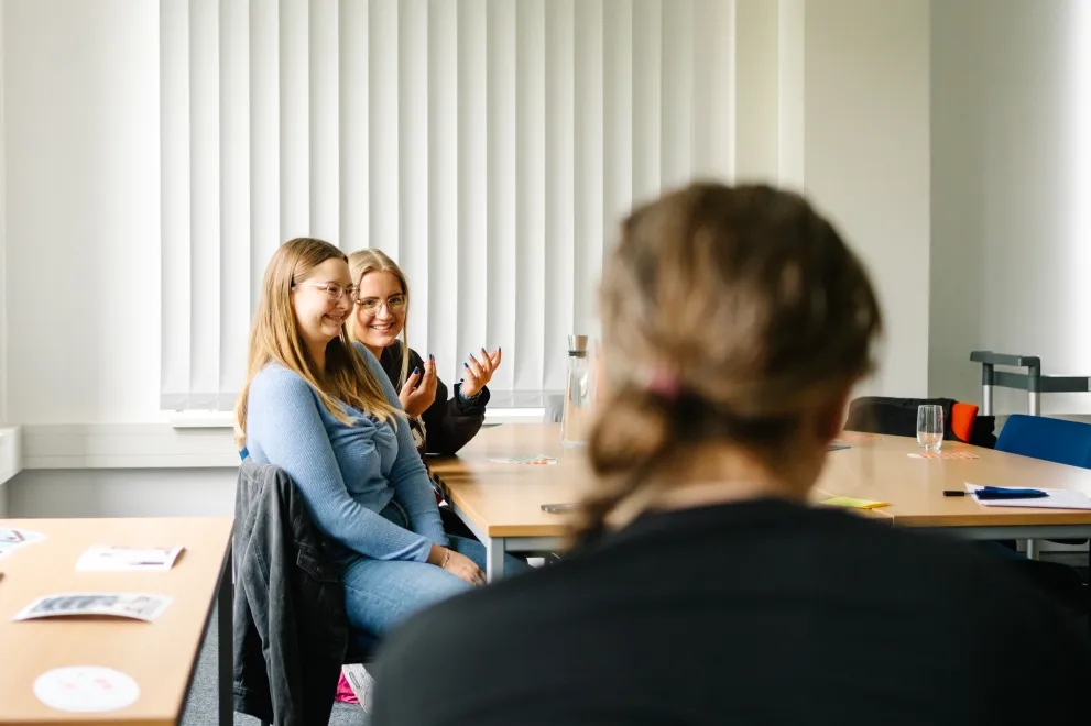 Foto: Drei Personen sitzen zusammen, lächeln und sprechen miteinander.