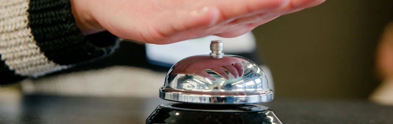 Klingel auf Platte, im Hintergrund eine Person, die auf die Klingel drückt.