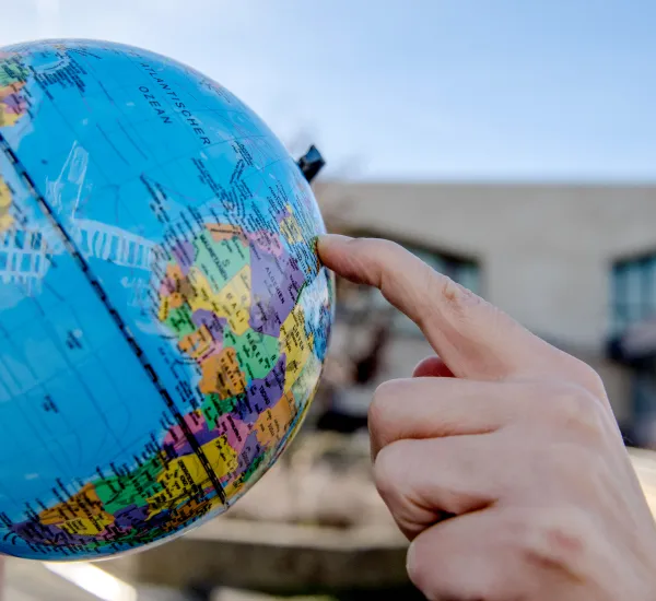 Foto: Eine Hand zeigt auf einen Globus, im Hintergrund der RUB-Campus.